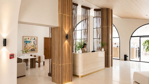 A modern reception area with a wooden reception desk, a dining area with a white table and chairs, and large windows offering views of the outside. - Marsa Boutique Hotel Marina El Alamein (El Alamein)