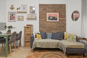 A cozy living room with a brick wall, a sofa with cushions, a dining table with chairs, and various framed artworks on the wall. - Casa Rubia Limón Holiday Home (Béznar)