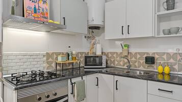 Une cuisine moderne avec des meubles blancs, une cuisinière à gaz, un four à micro-ondes et un évier.