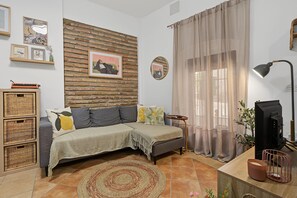 Una sala de estar acogedora con un sofá, una televisión, una lámpara y una pared de ladrillo.