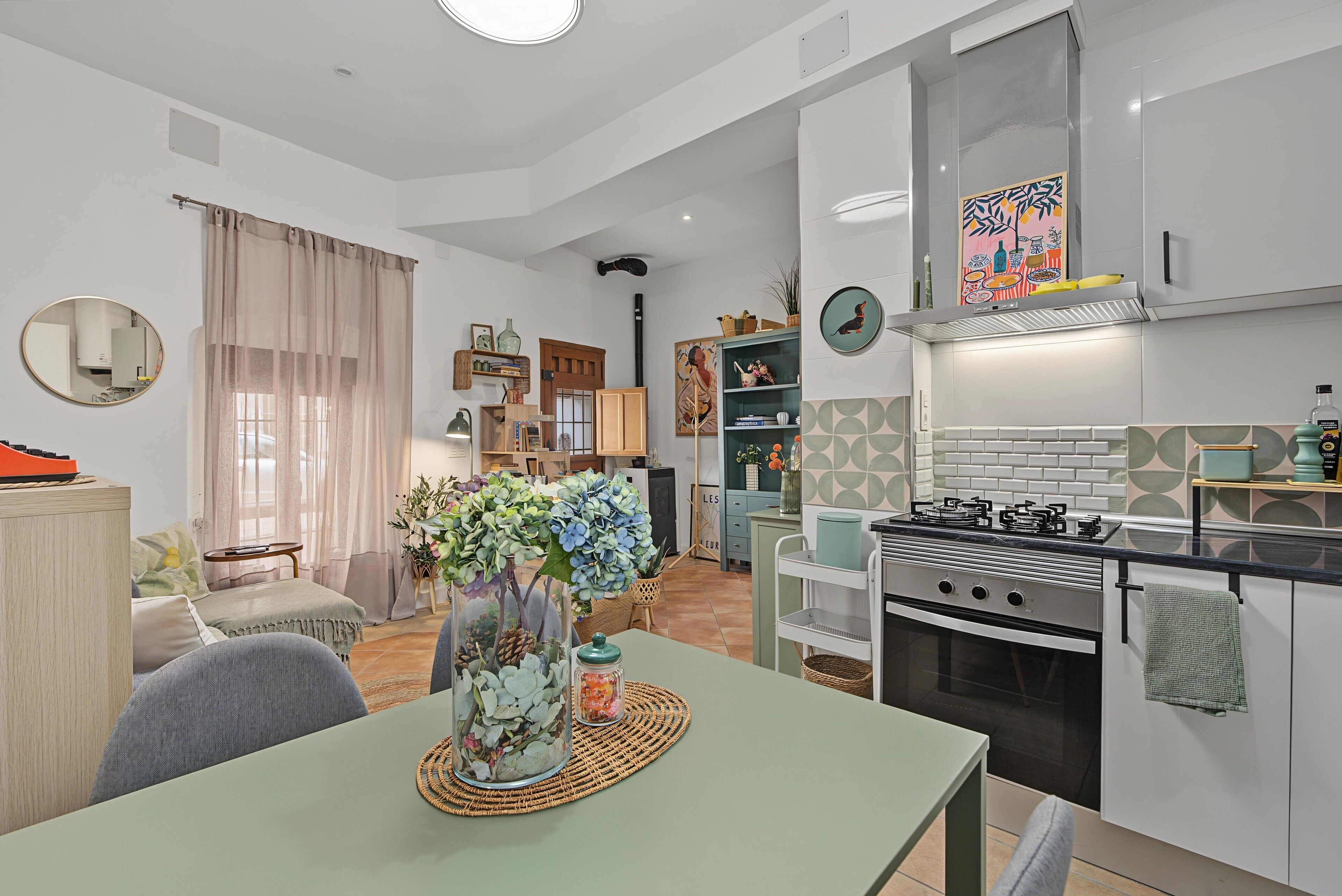 Eine moderne Küche mit Gasherd, ein Essbereich mit Tisch und Stühlen sowie ein Wohnzimmer mit Sofa und großem Fenster.