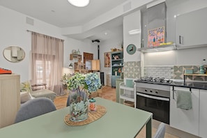 Eine moderne Küche mit Gasherd, ein Essbereich mit Tisch und Stühlen sowie ein Wohnzimmer mit Sofa und großem Fenster.