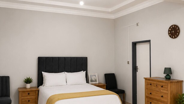 Un dormitorio con cama, mesitas de noche, cómoda, silla, puerta y un reloj de pared.