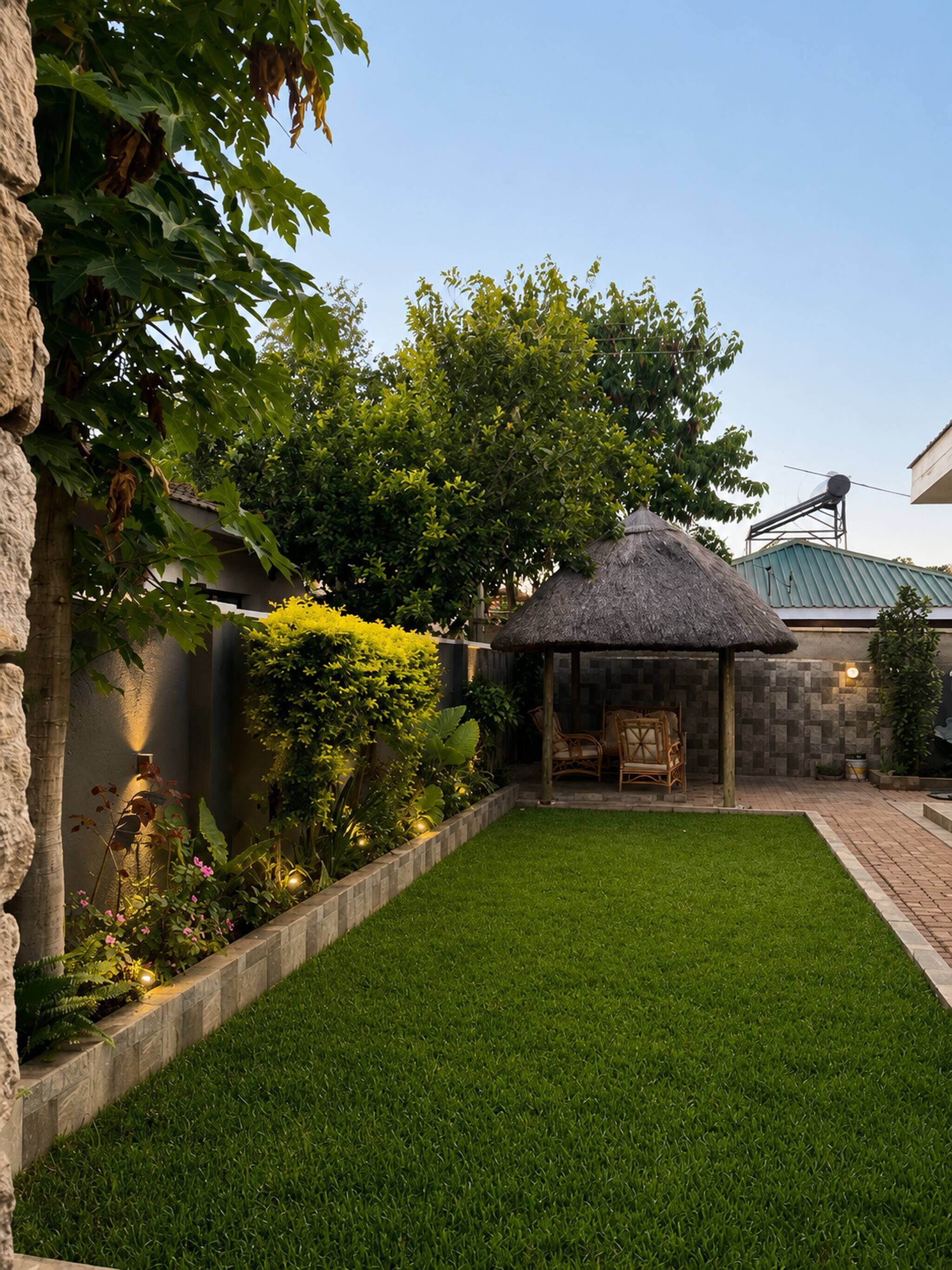 Un jardin bien entretenu avec un belvédère à toit de chaume, un mur de pierres et une pelouse verdoyante.