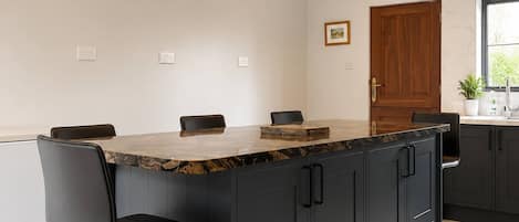 Una cocina moderna con una isla central, taburetes de bar, iluminación colgante y un reloj en la pared.