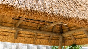 Un área de estar techada al aire libre con muebles de mimbre y techo de paja.