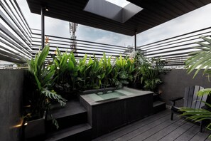 A rooftop terrace with a modern design, featuring a glass-enclosed hot tub, wooden flooring, and a variety of tropical plants. - Cyber Violet Studio @ Saigon's alley Rooftop Onsen (Thành phố Hồ Chí Minh)