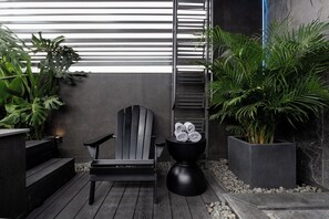 A modern outdoor seating area with a chair, a black table with towels, and potted plants. - Cyber Violet Studio @ Saigon's alley Rooftop Onsen (Thành phố Hồ Chí Minh)