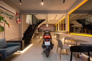 A motorcycle parked in a modern interior space with a staircase, seating area, and a dining table. - Cyber Violet Studio @ Saigon's alley Rooftop Onsen (Thành phố Hồ Chí Minh)