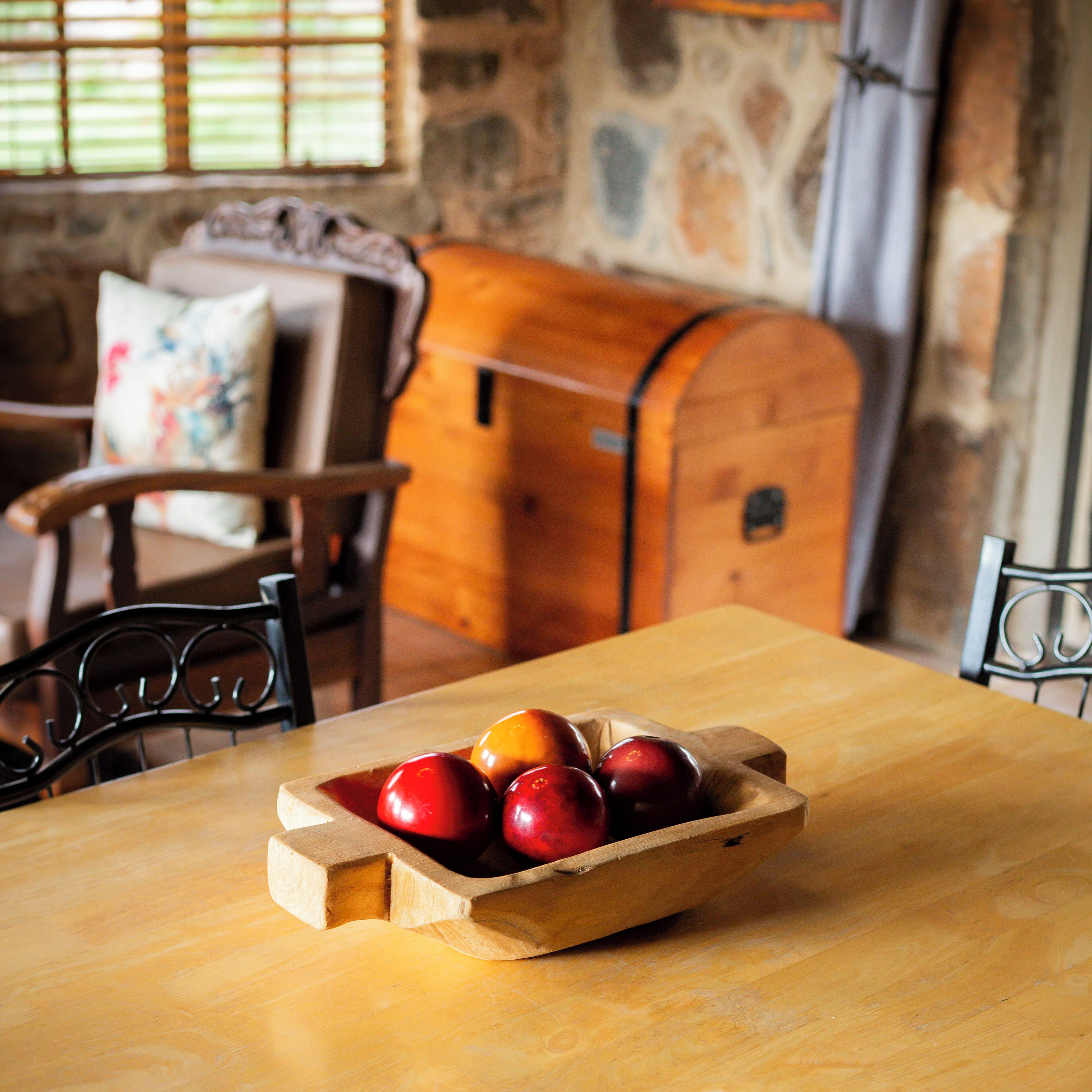 A wooden table with a fruit bowl containing apples and oranges.