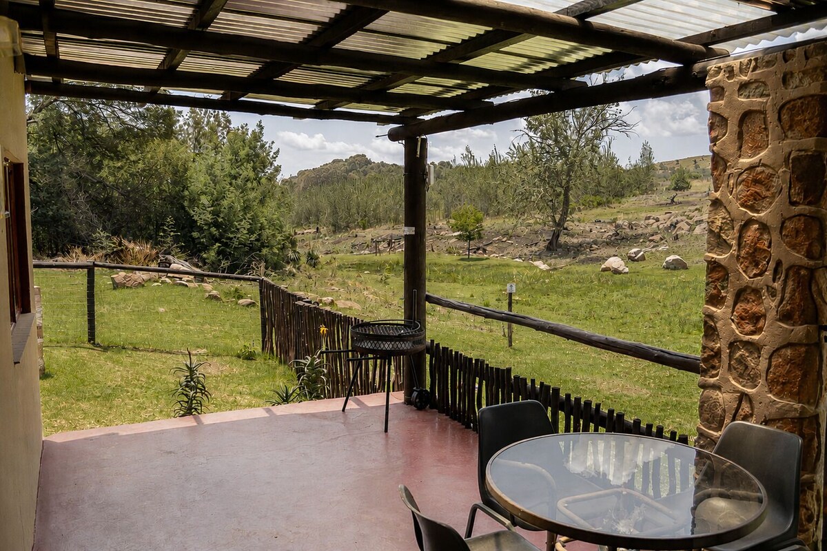 A covered outdoor seating area with a view of a grassy landscape and trees.
