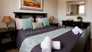 A neatly made bed with a pet-friendly linen option, two bedside lamps, a bedside table with a plant, and a mirror on the wall. - RIVERMAN CABIN COUNTRY LODGE (Tonteldoos)