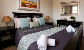 A neatly made bed with a pet-friendly linen option, two bedside lamps, a bedside table with a plant, and a mirror on the wall. - RIVERMAN CABIN COUNTRY LODGE (Tonteldoos)