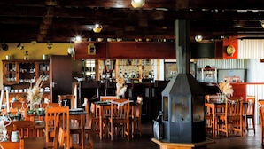 A restaurant interior with wooden tables and chairs, a bar area, and a central wood-burning stove. - RIVERMAN CABIN COUNTRY LODGE (Tonteldoos)