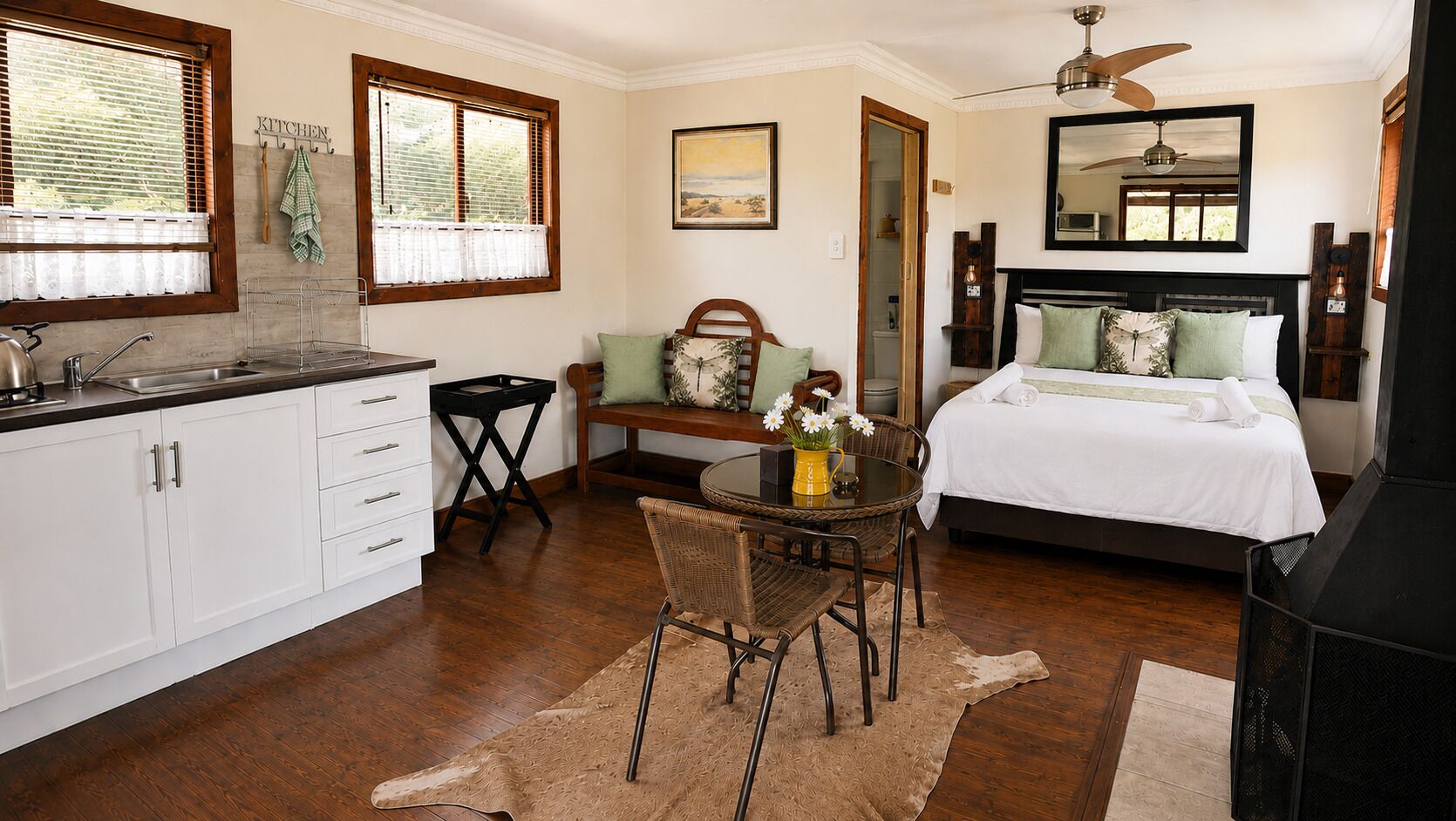 Una habitación con cama, una mesa de comedor con sillas, una zona de cocina y un ventilador de techo.