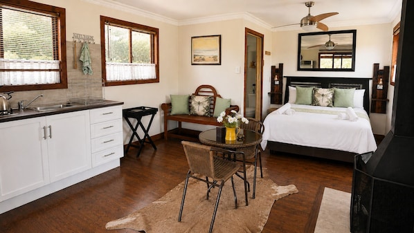A room with a bed, a dining table with chairs, a kitchen area, and a ceiling fan. - RIVERMAN CABIN COUNTRY LODGE (Tonteldoos)