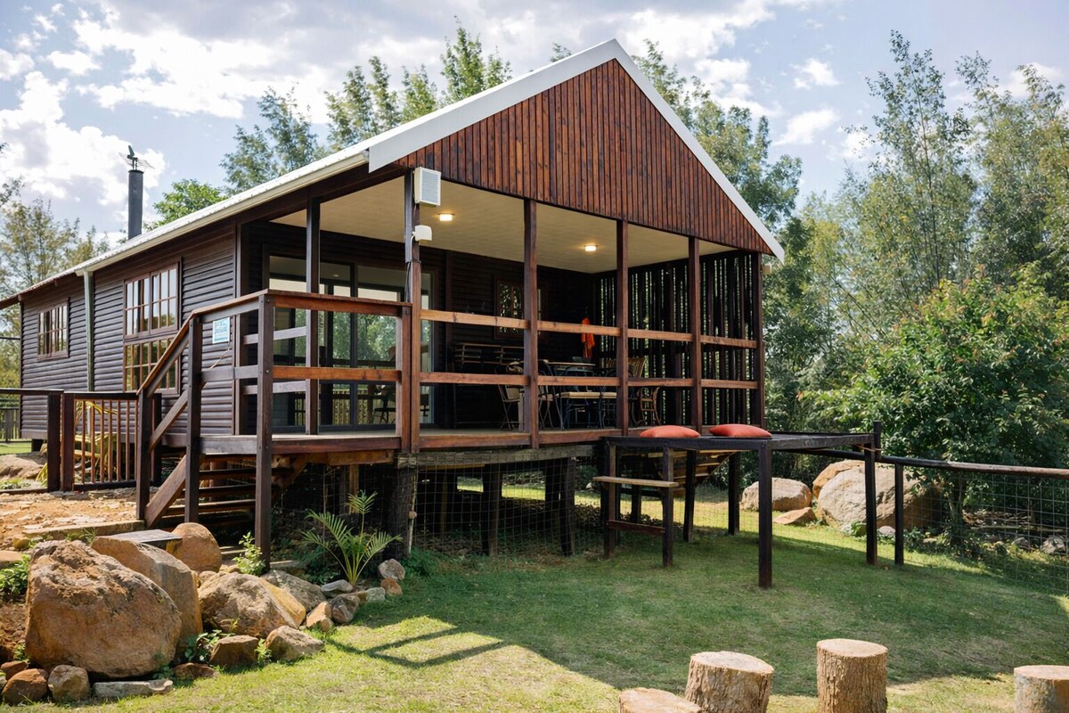 A wooden cabin with a balcony, large windows, and a fenced outdoor area.