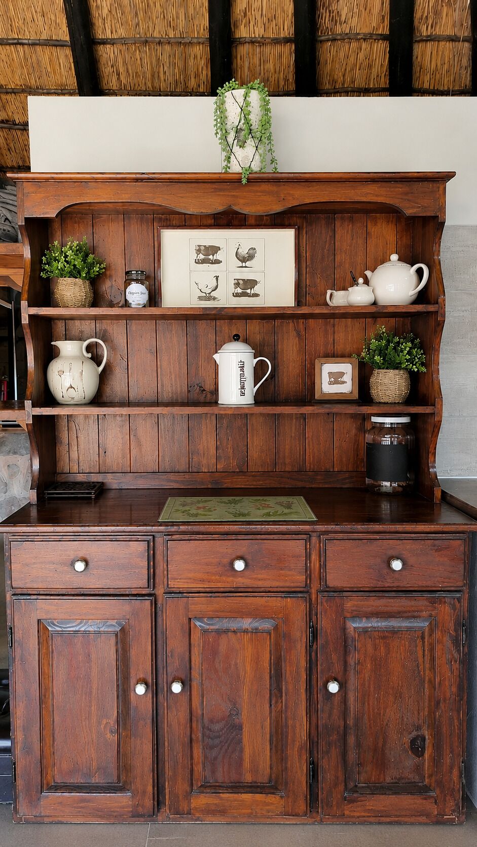 A wooden cabinet with drawers and shelves, decorated with plants and framed pictures.