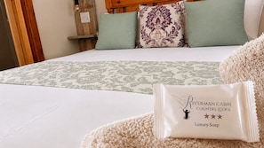 A neatly made bed with a patterned bedspread, a pillow with a floral design, and a package of luxury soap. - RIVERMAN CABIN COUNTRY LODGE (Tonteldoos)