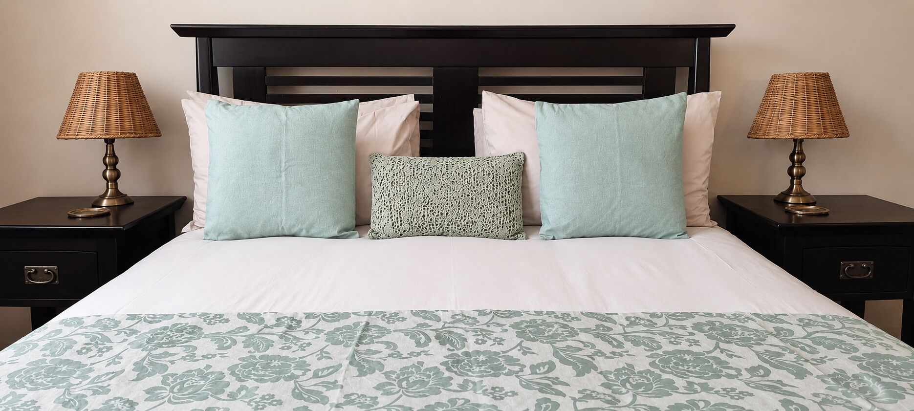 Un lit avec une couvre-lit à motifs floraux, une tête de lit sombre et deux tables de chevet dotées de lampes et de tiroirs.