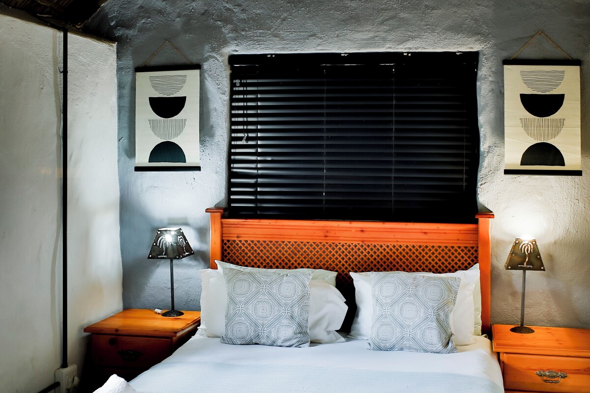 A bedroom with a wooden headboard, a large bed with white bedding, two bedside tables with lamps, and artwork on the walls.