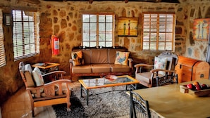A cozy living room with a stone wall, a leather sofa, a wooden table, and a vintage wooden cabinet. - RIVERMAN CABIN COUNTRY LODGE (Tonteldoos)