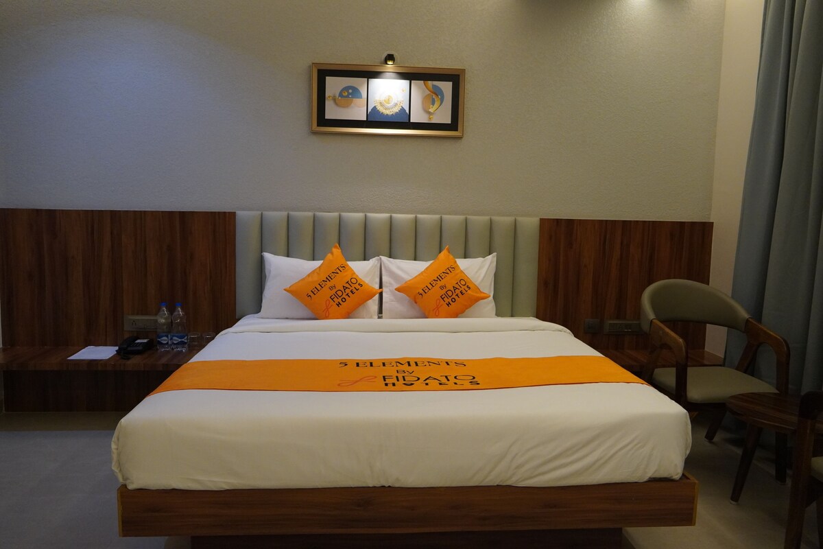 Una habitación de hotel con cama, dos almohadas, mesita de noche, silla y un cuadro en la pared.