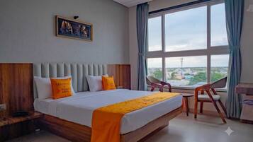 A hotel room with a large bed, a view of the city, a desk, and a chair.
