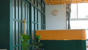 Et receptionsområde med grønne og gule farver, et ur på væggen og plantekrukker.