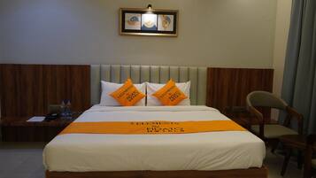 Habitació d'hotel amb un llit, dos almoiners, una tauleta de nit, una cadira i un quadre al mur.