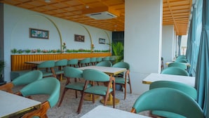 En restaurantindretning med grønne polstrede stole, hvide borde og et gult loft.