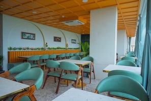 Un interior de restaurante con sillas tapizadas en verde, mesas blancas y techo amarillo.