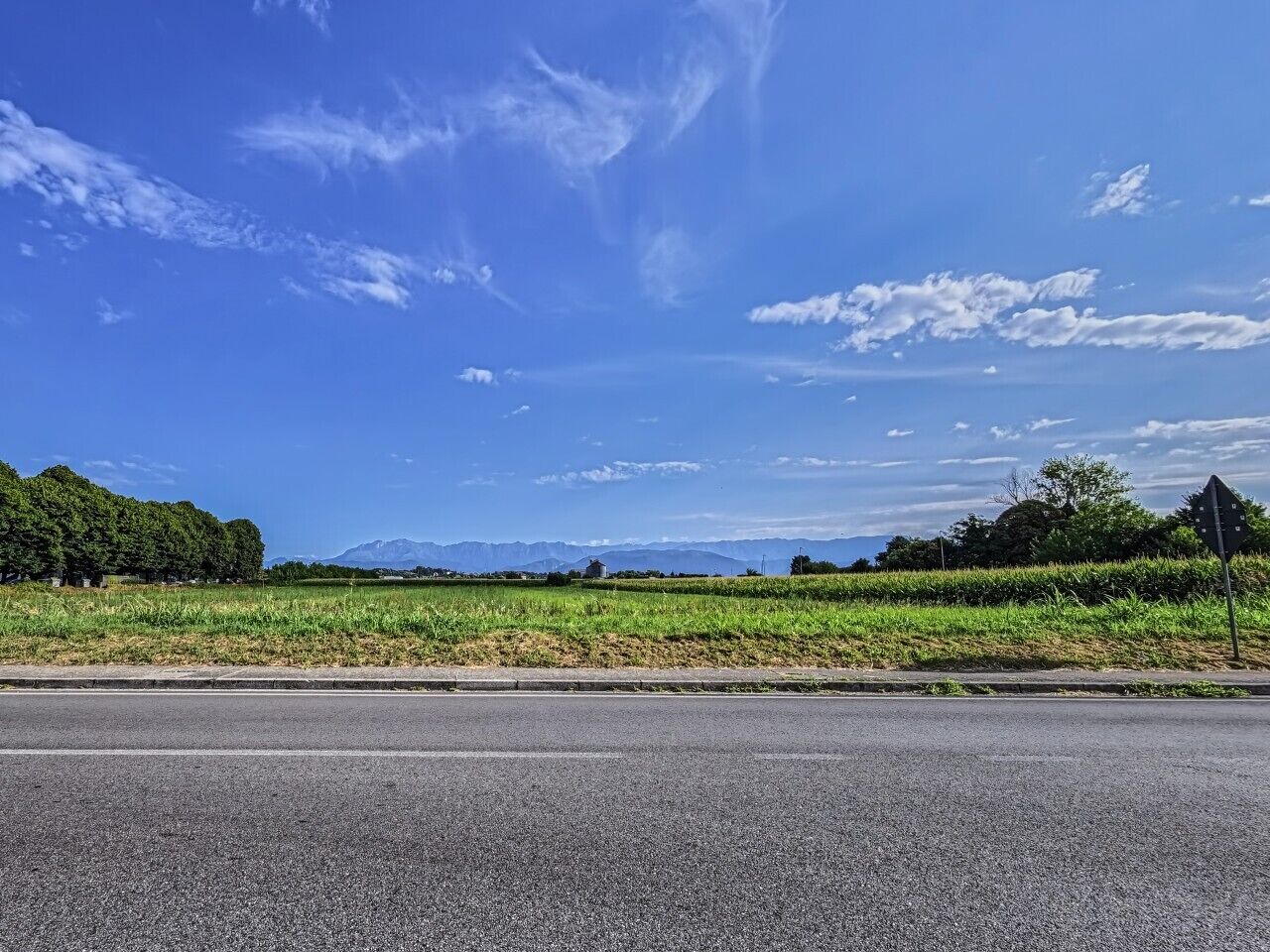 Een weg langs een grasveld, met een bergketen in de verte.