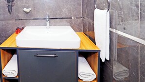 A bathroom with a white sink, dark marble walls, a wooden vanity, a towel rack, and a mirror. - ARGES SUİTE HOTEL (istanbul)