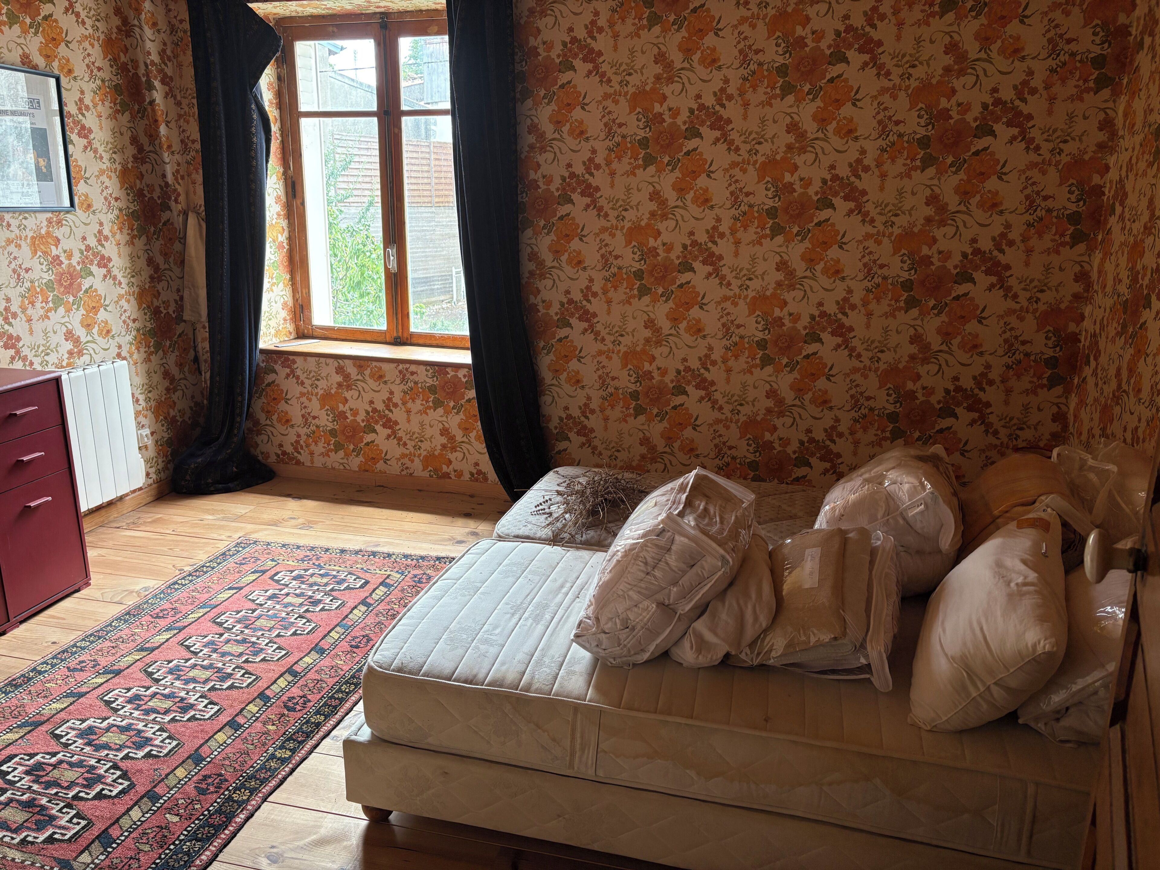 A bedroom with a bed, a radiator, a window with curtains, and a patterned rug.