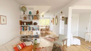 Ein gemütliches Wohnzimmer mit einer Couch, einem Bücherregal, einem Essbereich mit Stühlen und Holzboden.