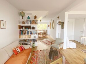 Ein gemütliches Wohnzimmer mit einer Couch, einem Bücherregal, einem Essbereich mit Stühlen und Holzboden.