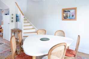 Ein Essbereich mit weißem Tisch, Korbstühlen, einem gemusterten Teppich und einer Treppe.