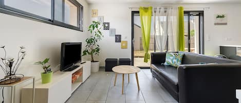 A modern living room with a flat-screen TV, a sofa, a coffee table, and a potted plant.