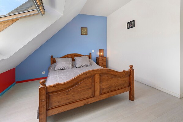 A bedroom with a sloped ceiling, a wooden bed, a bedside lamp, and a small wall clock.