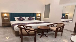 Une chambre d’hôtel avec un lit, deux chaises en bois, une petite table ronde et un miroir au mur.