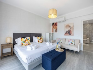 A modern hotel room with a large bed, a sofa, a small side table, and a blue ottoman. - Solmonte Apartment - Pool Access, Beach Close (Portimão)