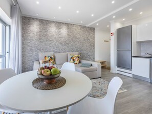 A modern living room with a dining table, a sofa set, and a kitchen area with a built-in fridge. - Solmonte Apartment - Pool Access, Beach Close (Portimão)