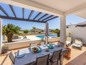 A dining area with a table set for four, overlooking a swimming pool and a hillside. - Casa Iguana - Village Apartment with Shared Pool (Budens)