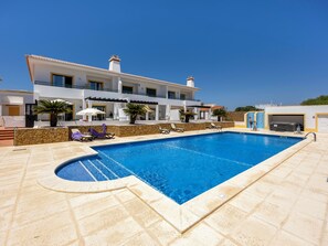 A swimming pool with lounge chairs and umbrellas, a stone wall, and a building with balconies. - Casa Iguana - Village Apartment with Shared Pool (Budens)