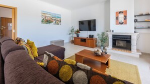Ein modernes Wohnzimmer mit Sofa, Couchtisch, Fernseher, Kamin und Blick ins Freie.