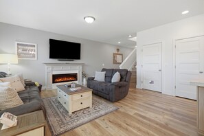 A living room with a fireplace, a sofa, a coffee table, and a television. - Page Place: Modern Extended Stay in Newberg, Dog-Friendly (Newberg)