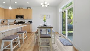 A modern kitchen with wooden cabinets, a stainless steel microwave, and a dining area with a table and chairs. - Page Place: Modern Extended Stay in Newberg, Dog-Friendly (Newberg)