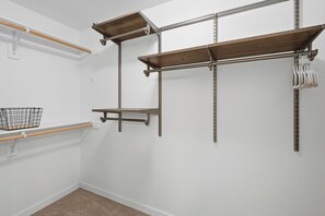 Ein Zimmer mit weißer Wand, einem Holzregal, einem Metallgestell und einem weißen Teppich.
