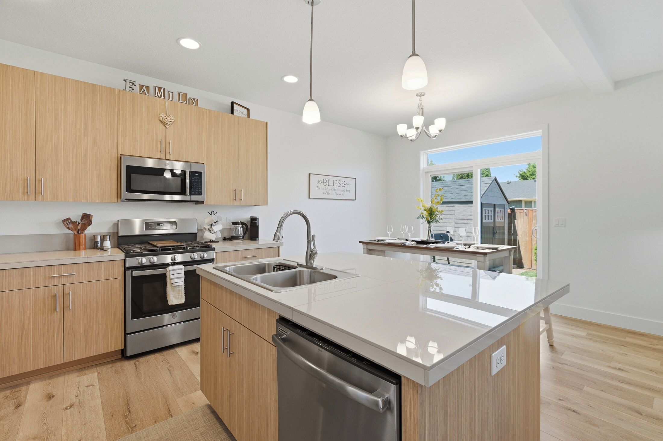 Une cuisine moderne avec des meubles en bois, des appareils en acier inoxydable, un grand îlot central et des luminaires suspendus.